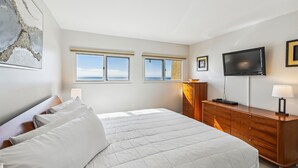 A bedroom with a bed, a dresser, a TV, and two windows with a view of the sea. - Beach House 303B is Beautiful Gulf Front 2 BR with Free Beach Service for 2 (Miramar Beach)