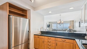 A modern kitchen with a stainless steel refrigerator, wooden cabinets, and a black countertop. - Beach House 303B is Beautiful Gulf Front 2 BR with Free Beach Service for 2 (Miramar Beach)
