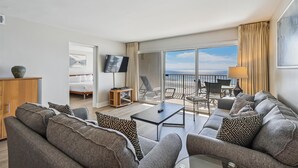 A modern hotel room with a balcony, a sofa set, a TV, and a bed. - Beach House 303B is Beautiful Gulf Front 2 BR with Free Beach Service for 2 (Miramar Beach)