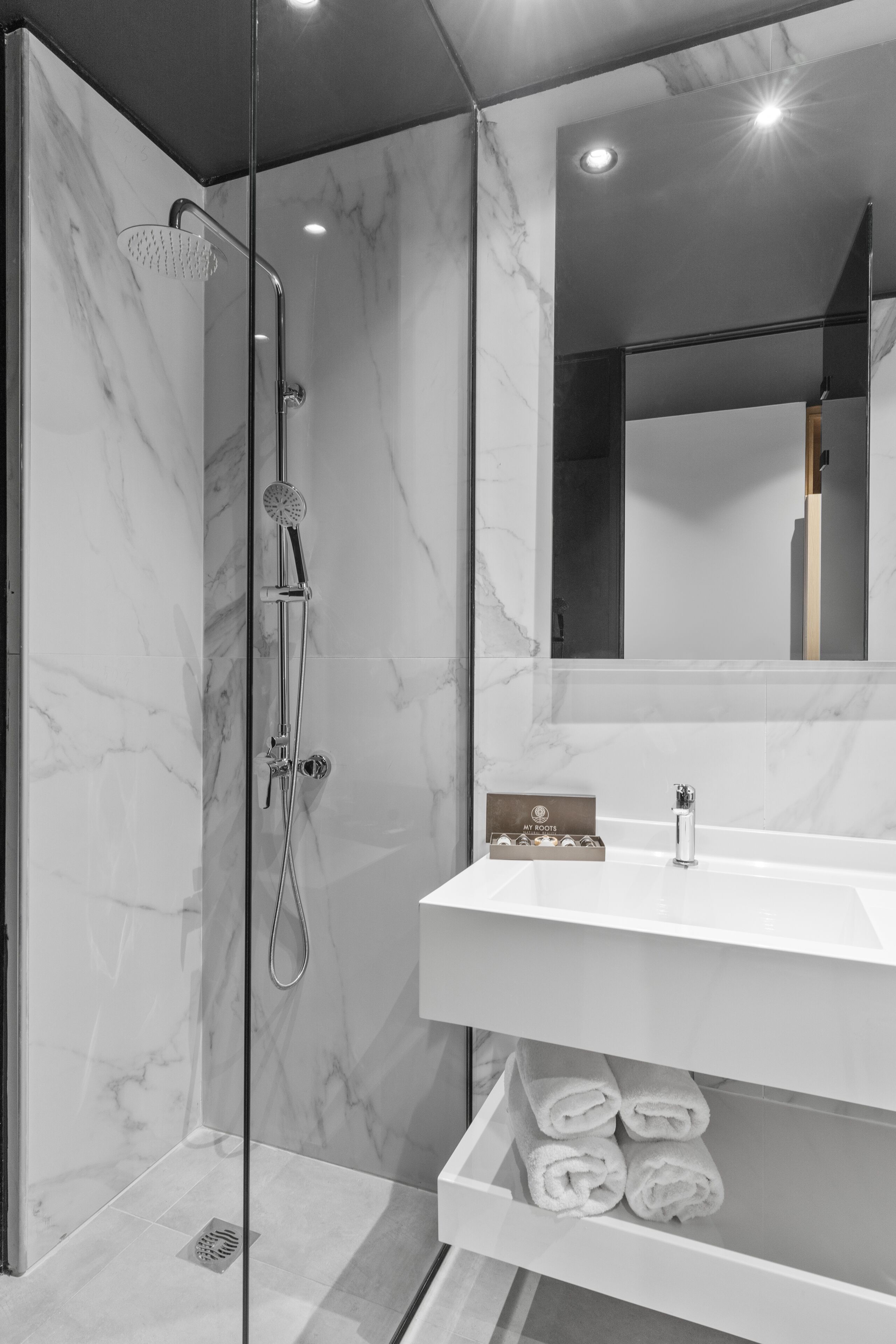 Un baño moderno con ducha de vidrio, tocador blanco y espejo sobre el lavabo.
