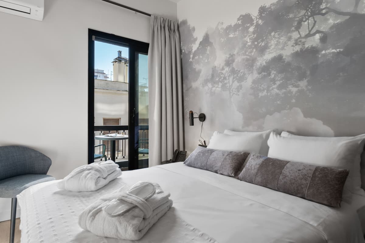 A hotel room with a bed, a chair, a view through a glass door, and a wall mural.