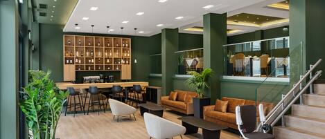 A modern lobby with a bar area, seating, and a staircase.