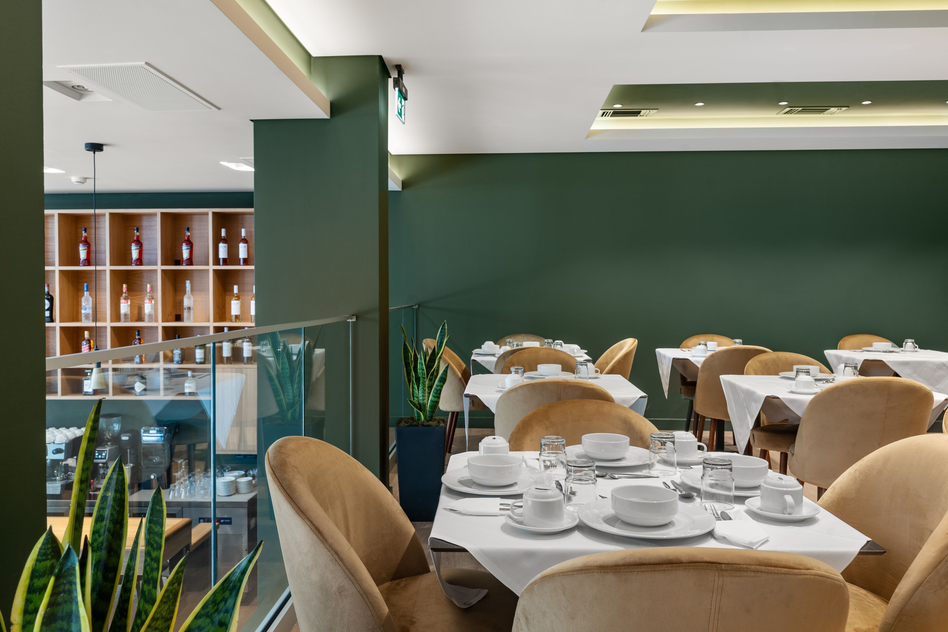 Un ristorante con tavoli apparecchiati, una zona bar con bottiglie e vista sulla città attraverso una parete di vetro.