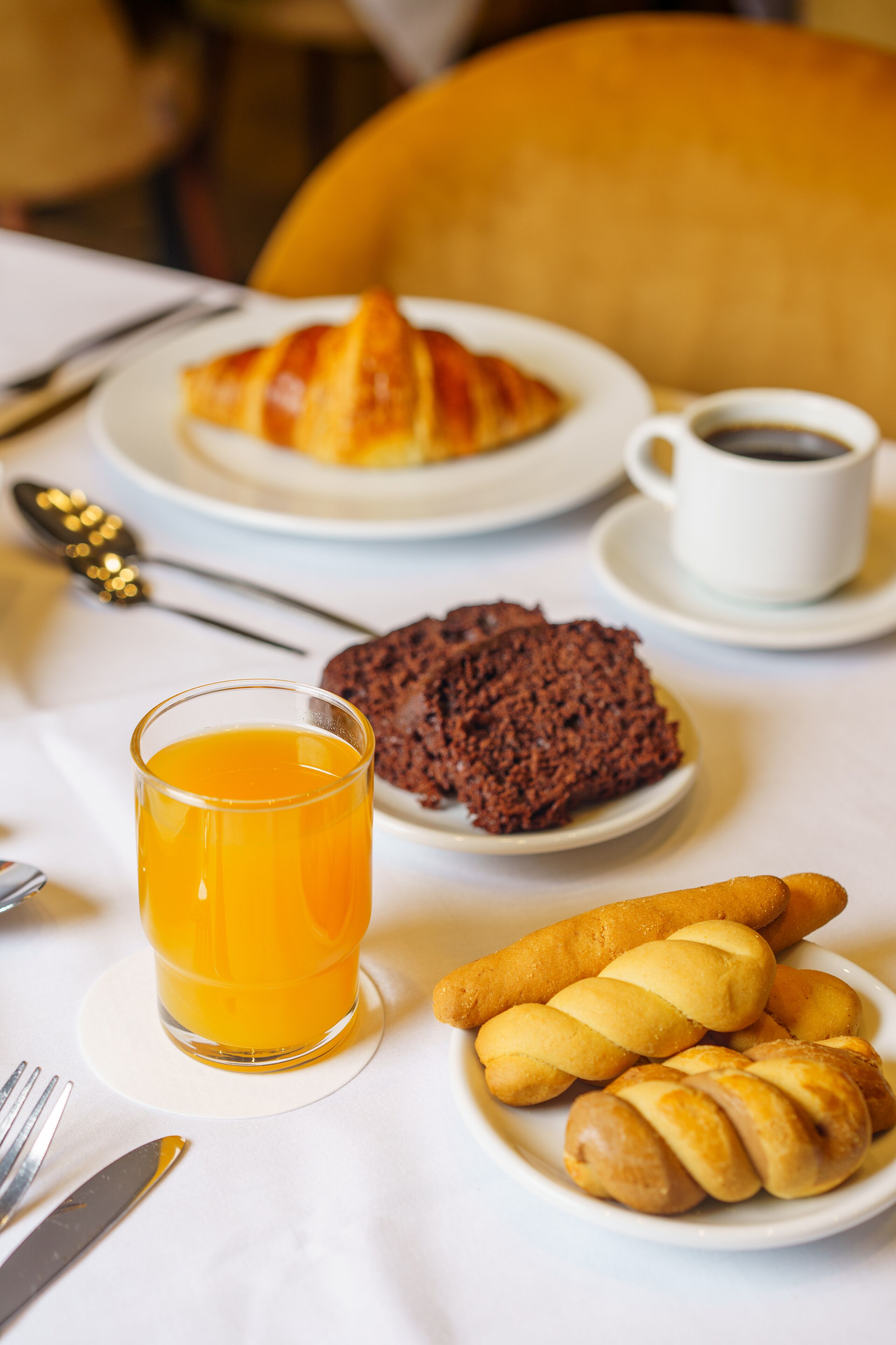 Ein Frühstückstisch mit Croissants, Schokoladenkuchen, Orangensaft und Kaffee.