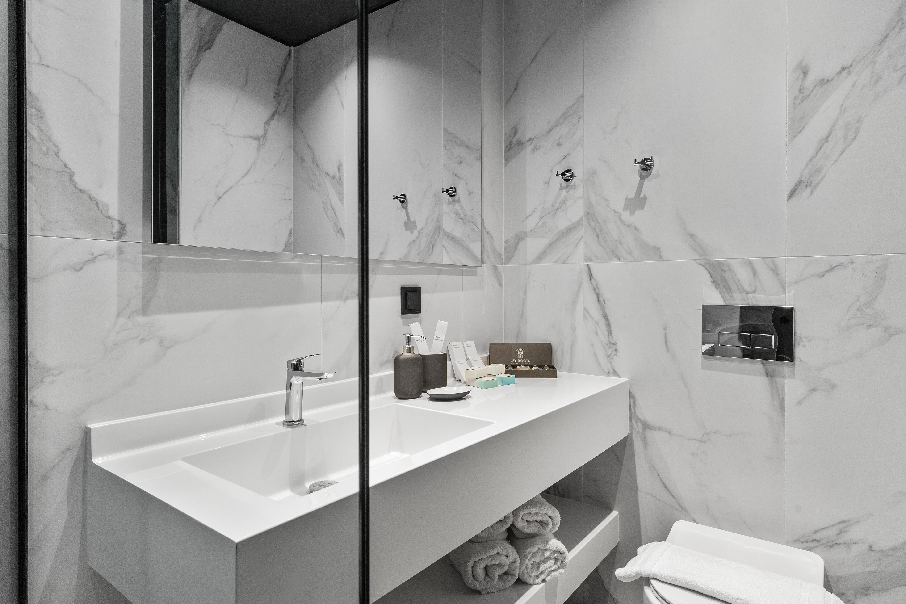 A modern bathroom with a white marble sink, a large mirror, and a towel rack.
