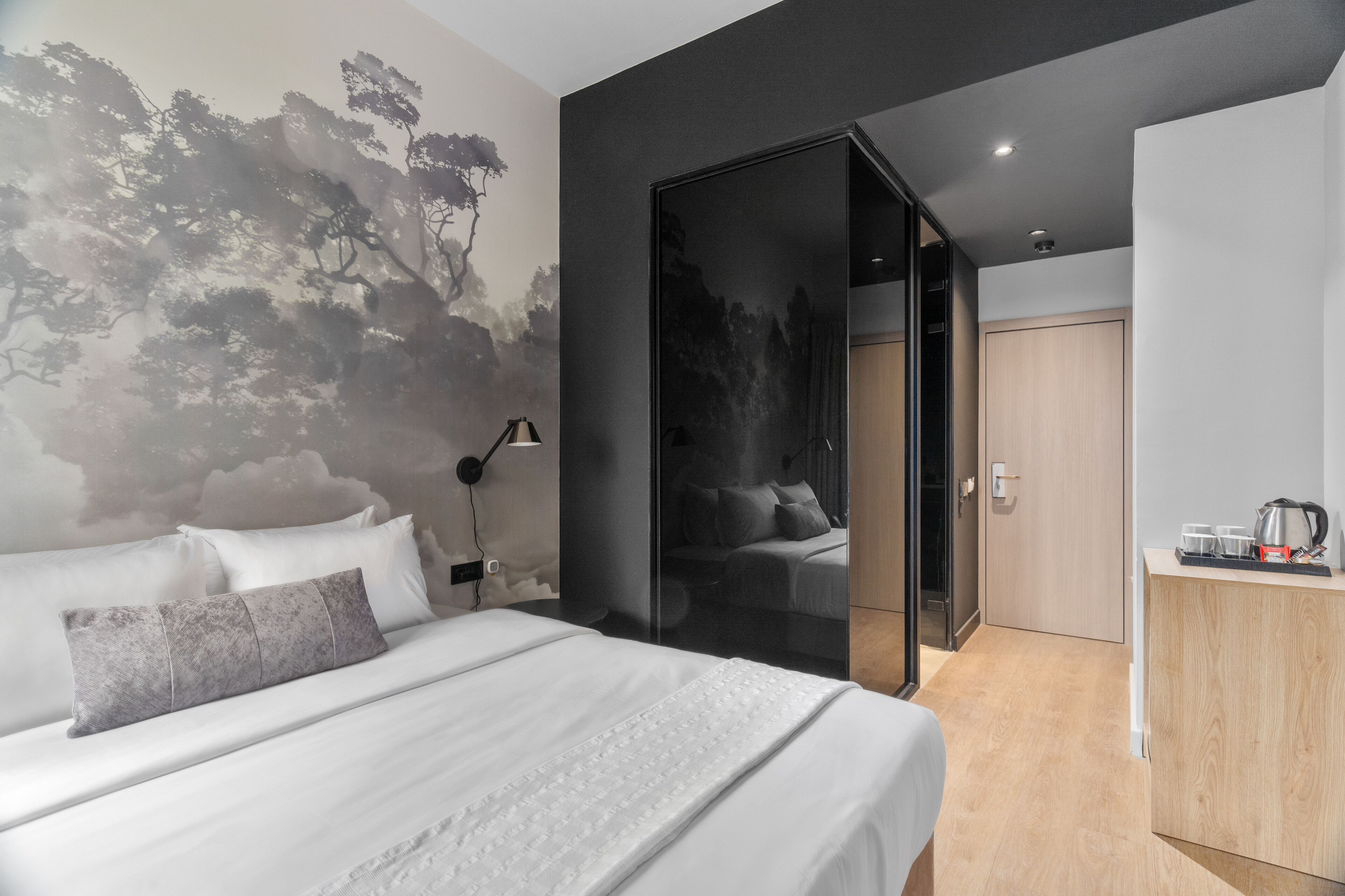 A modern hotel room with a large bed, a desk with a kettle, and a wardrobe.