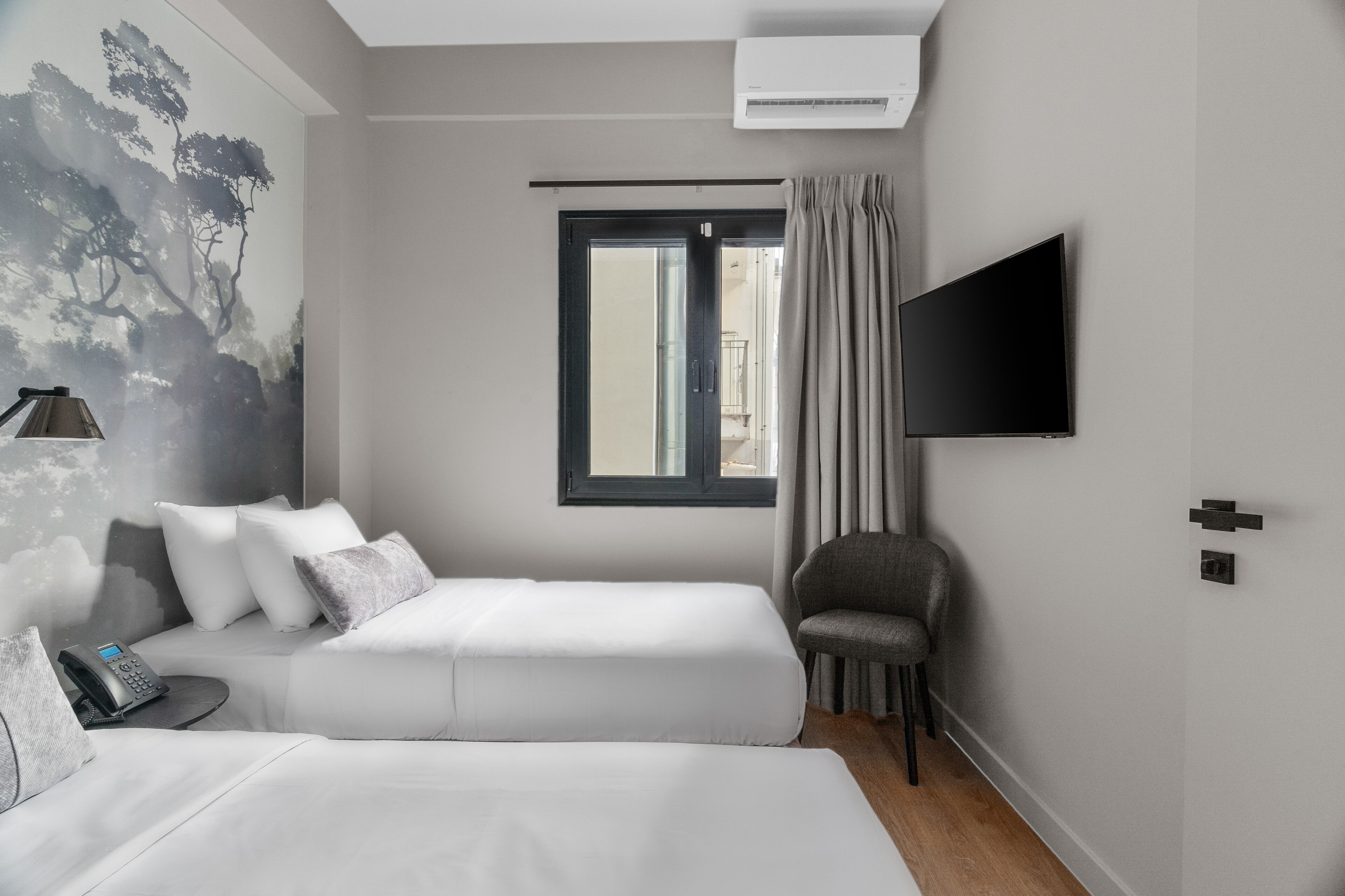 A modern hotel room with two beds, a flat-screen TV, a window with curtains, a chair, and a wall-mounted phone.
