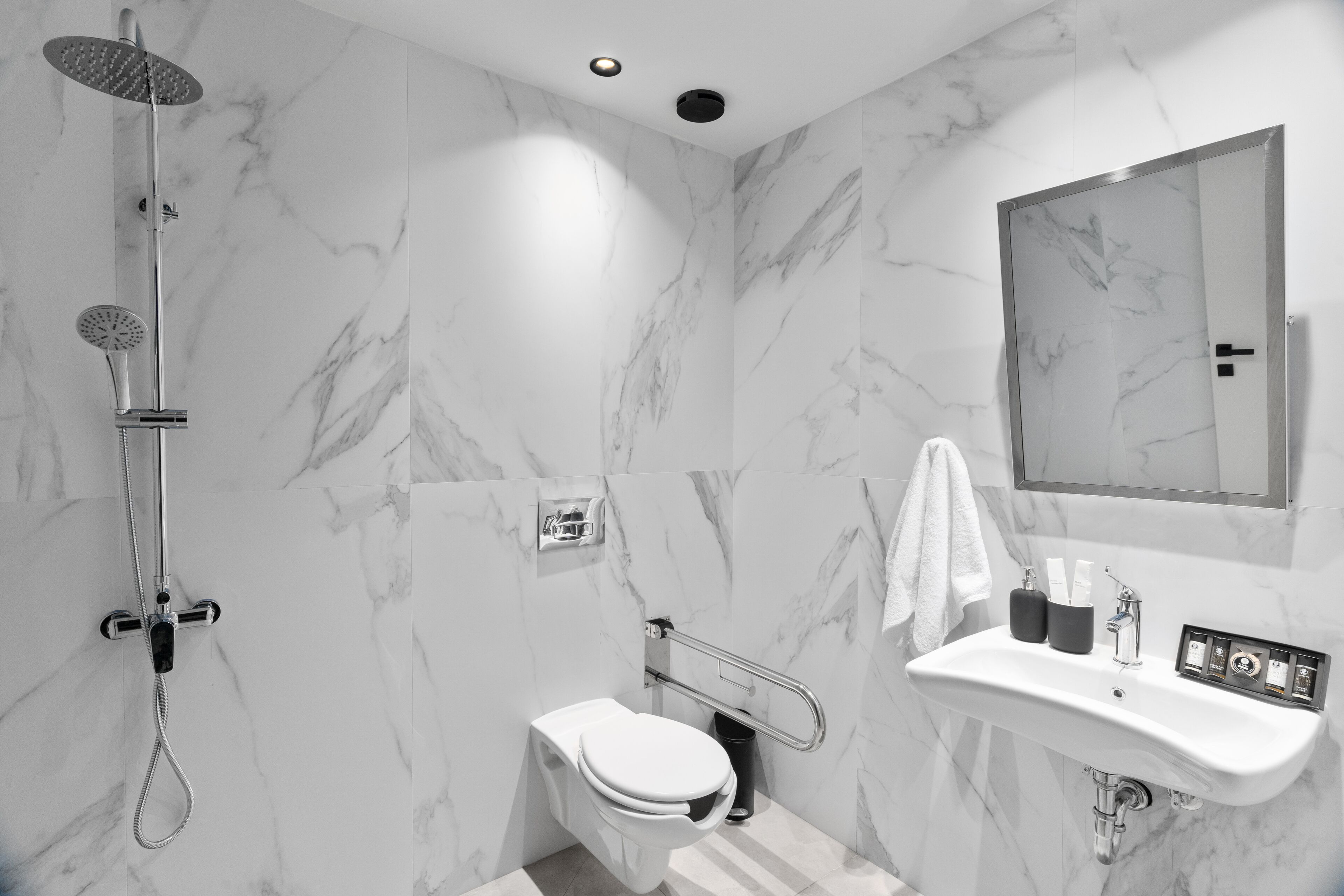 Un baño moderno con pared de mármol, ducha, inodoro y lavabo con artículos de aseo.