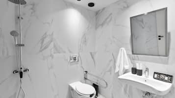 Un baño moderno con pared de mármol, ducha, inodoro y lavabo con artículos de aseo.
