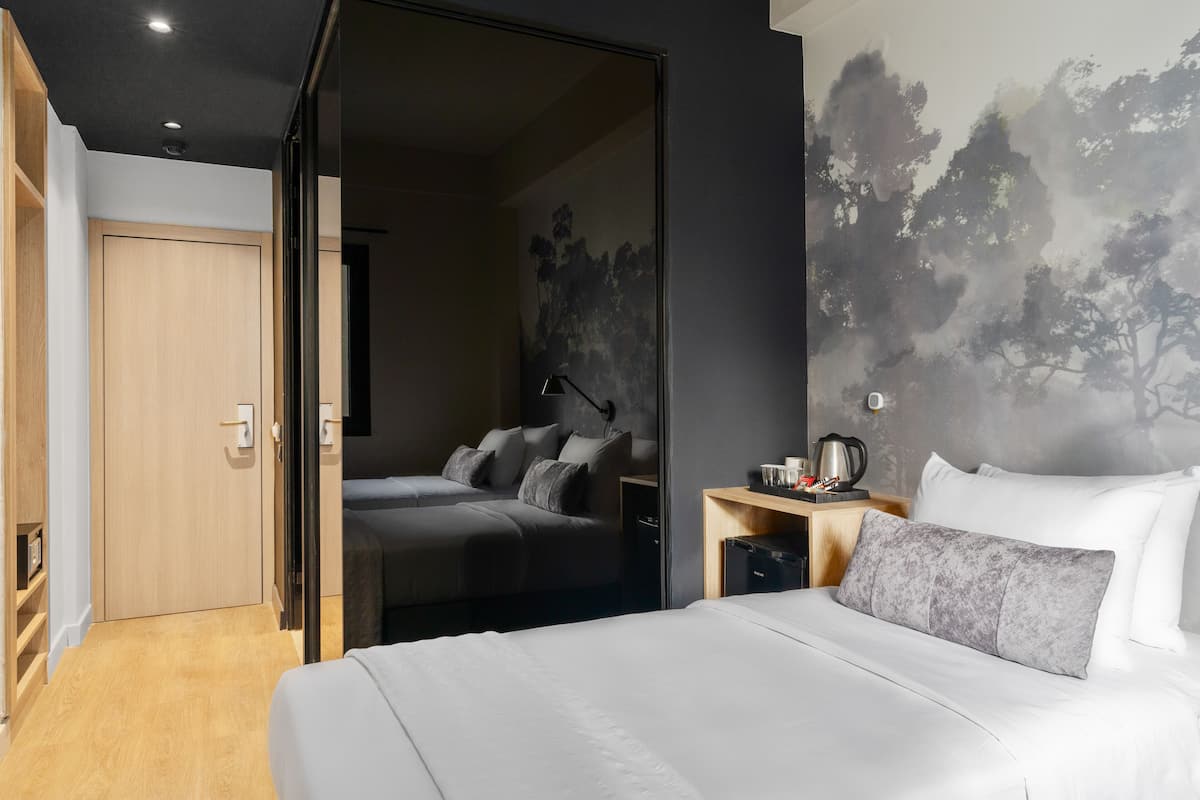 A hotel room with a bed, a desk with a lamp, and a painting on the wall.