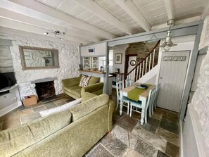 A cozy living room with a stone fireplace, a green sofa, and a dining area with a wooden table and chairs.