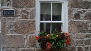 A stone building with a white window and a flower box containing red and yellow flowers. - Trelonie - a Fisherman's Cottage in St Ives Town (St Ives)