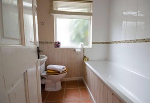 A small bathroom with a toilet, a window, and a bathtub.