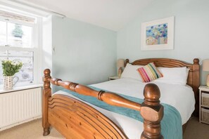 A bedroom with a wooden bed, a window with a view, a bedside table, and a wall-mounted painting.