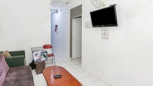Um espaço de estar pequeno e aconchegante, com sofá, mesa de madeira e televisão fixada na parede.