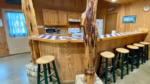 Cucina con mobili in legno, isola centrale con sgabelli e un grande tronco d'albero come elemento decorativo.