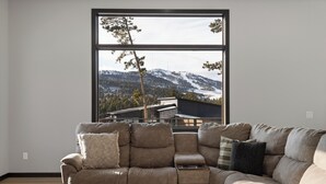 A modern living room with a large window, a sectional sofa, and a round coffee table. - Incredible View, Open Floor Plan, Paved Roads, Hot Tub, Access to Clubhouse! (Lead)