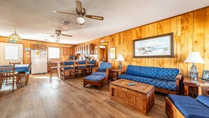 A wooden interior with a dining area, kitchen, and seating area. - The Beach Box - Kitty Hawk MP 4.5, Ocean View, 240 Yds to Beach, Pets OK, Flex Stays (Kitty Hawk)