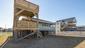 A building with a wooden deck structure, a covered area with stairs, and a fenced yard. - The Beach Box - Kitty Hawk MP 4.5, Ocean View, 240 Yds to Beach, Pets OK, Flex Stays (Kitty Hawk)