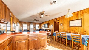 A wooden interior with a kitchen, dining area, and a ceiling fan. - The Beach Box - Kitty Hawk MP 4.5, Ocean View, 240 Yds to Beach, Pets OK, Flex Stays (Kitty Hawk)