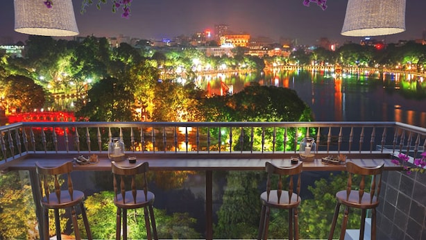 Terraza con mesa y sillas con vista a un río y edificios iluminados.