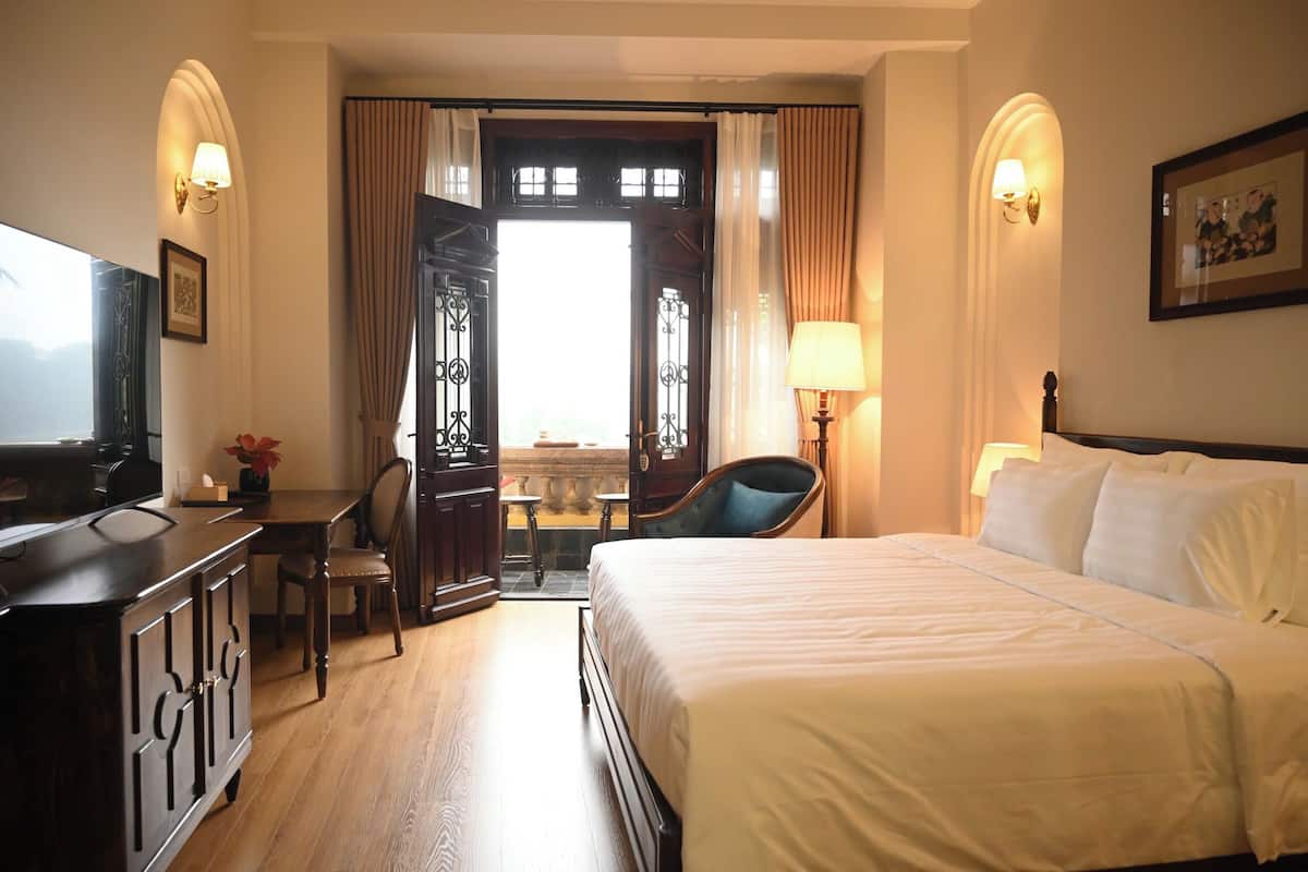Une chambre d’hôtel avec un lit, un bureau et une chaise, une télévision et une fenêtre avec des rideaux.