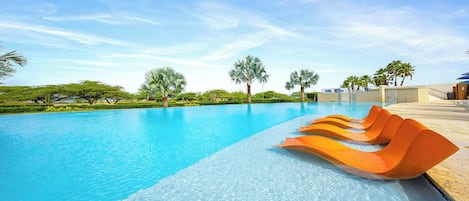 Piscina cristalina con varios sillones anaranjados, rodeada de follaje y palmeras.