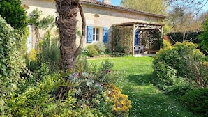 Una casa rústica con jardín, una pérgola y una pequeña zona de estar al aire libre.