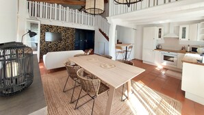 Amplia sala de estar con una mesa de comedor de madera, sillas de mimbre, un sofá y una escalera que sube a un nivel superior.