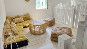 Una habitación acogedora con un sofá amarillo, otomanas de mimbre y una lámpara de pie trenzada.
