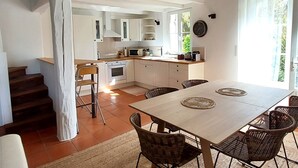 Una cocina amplia con armarios blancos, una mesa de comedor con sillas de mimbre y una escalera que sube a un nivel superior.