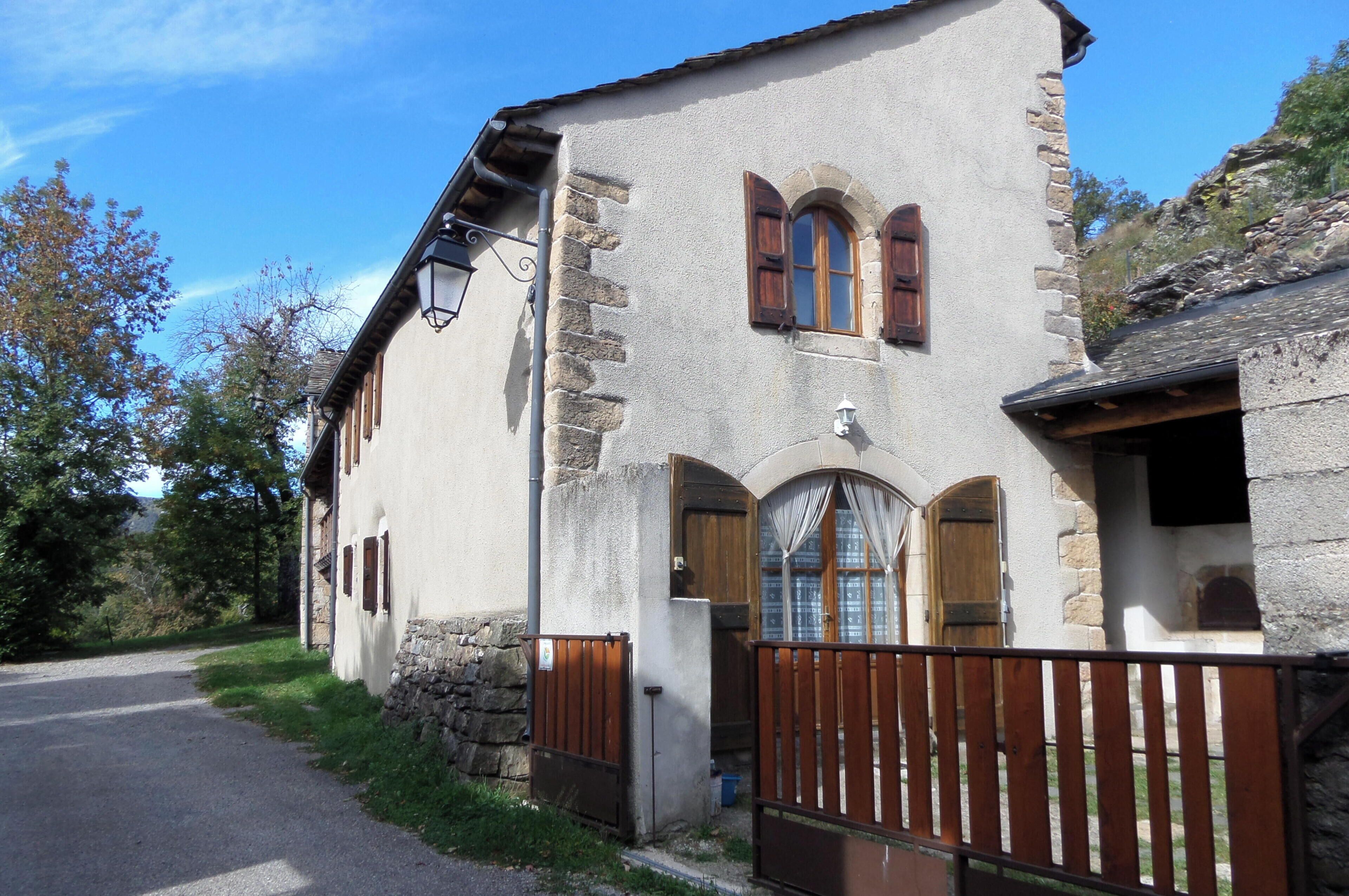 A stone building with a wooden gate, a paved road, and trees in the background.