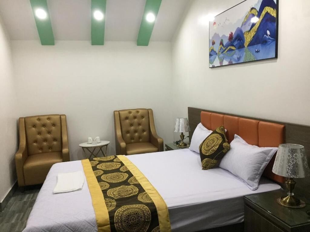 A hotel room with a bed, two armchairs, a small table, and a nightstand.