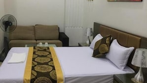 A hotel room with a bed, a nightstand, a lamp, a fan, a sofa, and a painting on the wall. - Anh Sao Hotel by Bay Luxury (Hanoi)
