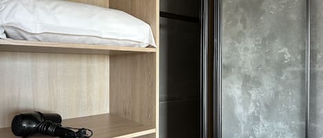 Una camera da letto con un armadio in legno, un letto con biancheria bianca e un asciugacapelli nero su uno scaffale.