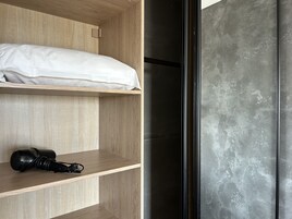 Un dormitorio con un armario de madera, una cama con ropa blanca y un secador de pelo negro en un estante.