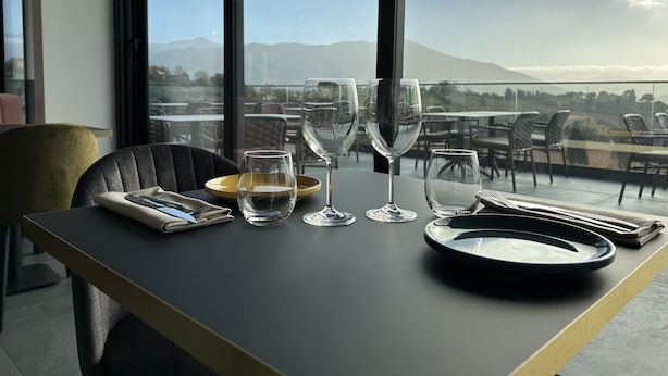 A dining table set with plates, glasses, and cutlery, overlooking a scenic view with mountains and a body of water. - Hôtel Casa Matteu (Afa)