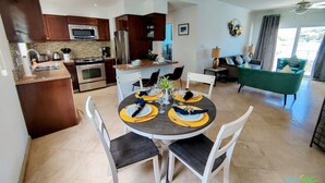 Une cuisine moderne avec des meubles de couleur bois foncé, des appareils électroménagers en acier inoxydable et un coin repas doté d’une table ronde pour quatre personnes.