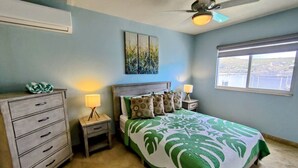 Une chambre à coucher comprenant un lit, des tables de chevet, une commode, un ventilateur de plafond et une fenêtre donnant sur un paysage agréable.