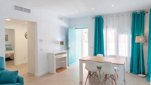 Ein modernes Zimmer mit Esstisch, Stühlen und Schreibtisch. Eine Tür führt in einen anderen Raum, ein Fenster mit Vorhängen.