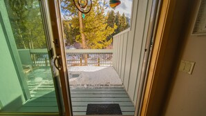 A wooden deck with a metal railing, a glass door leading outside, and a doormat on the deck. - Summer Escape | Balcony, Listen to River & Views (Keystone)