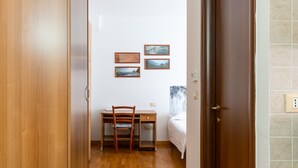 Une pièce comprenant une armoire en bois, un bureau avec une chaise, un lit et deux tableaux encadrés accrochés au mur.