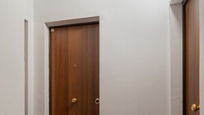 Un couloir avec une porte en bois, un paillasson et un sol carrelé.