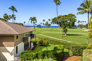 Un campo de golf con vista al océano, palmeras y un edificio con balcón.