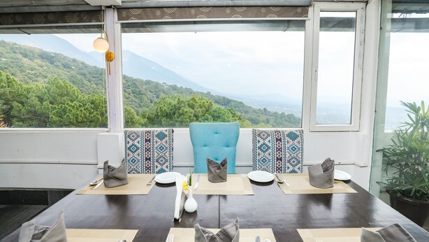 A dining table set for four with a view of green hills and mountains. - Saalak Lite Eliot Exotica  (Dharamshala)