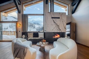 A cozy room with a fireplace, large windows with a snowy mountain view, and comfortable seating.