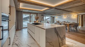 Una cocina moderna con una isla grande, vigas de madera en el techo y una zona de comedor con mesa y sillas.
