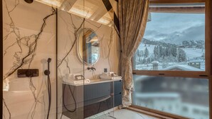 A bathroom with a marble wall, a large mirror, and a view of a snowy landscape through a window.