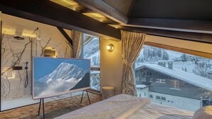 A bedroom with a large bed, a television displaying a snowy mountain, and a view of a snowy village through the window.