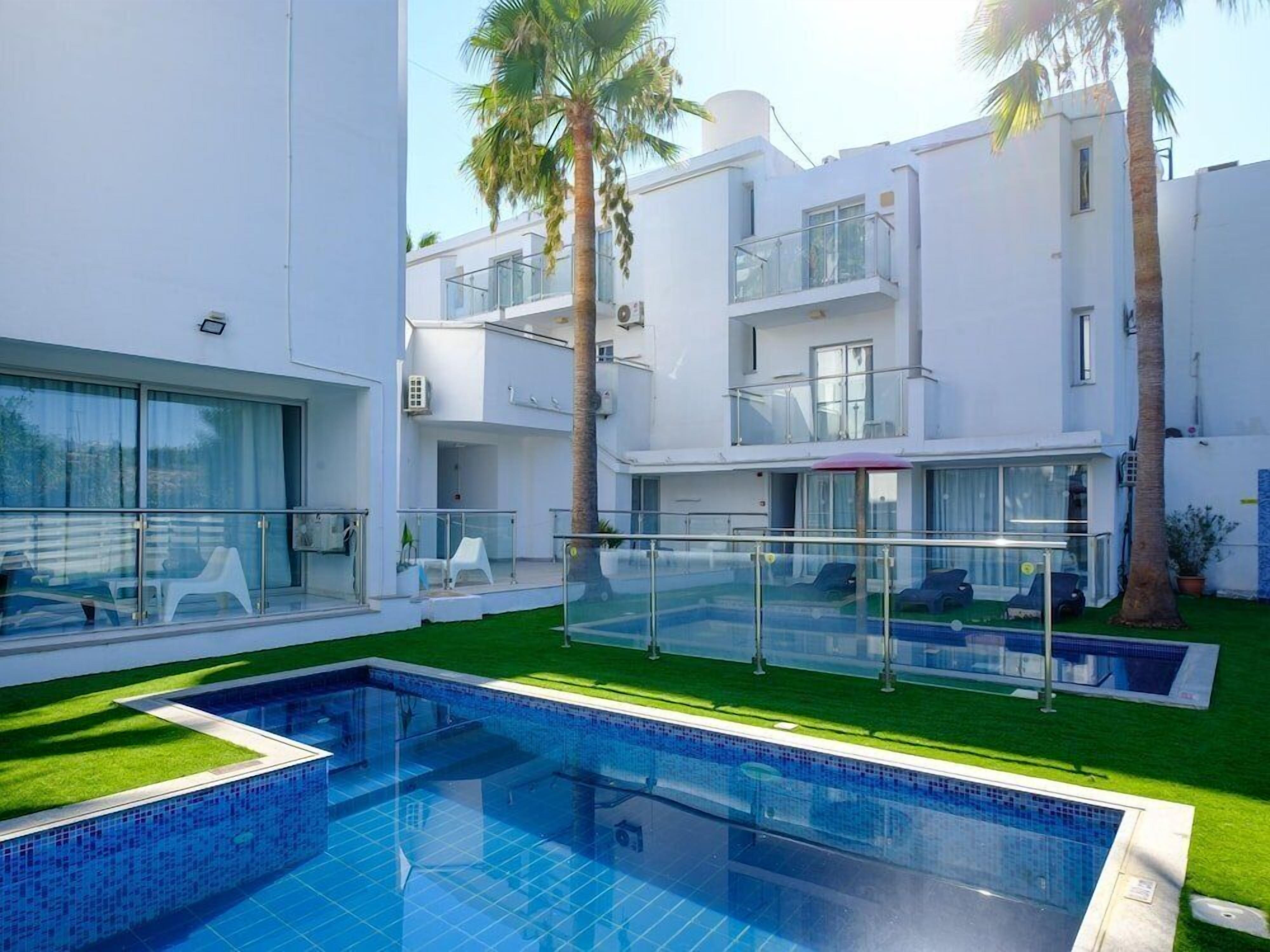 A modern hotel with a swimming pool, outdoor seating, and palm trees.
